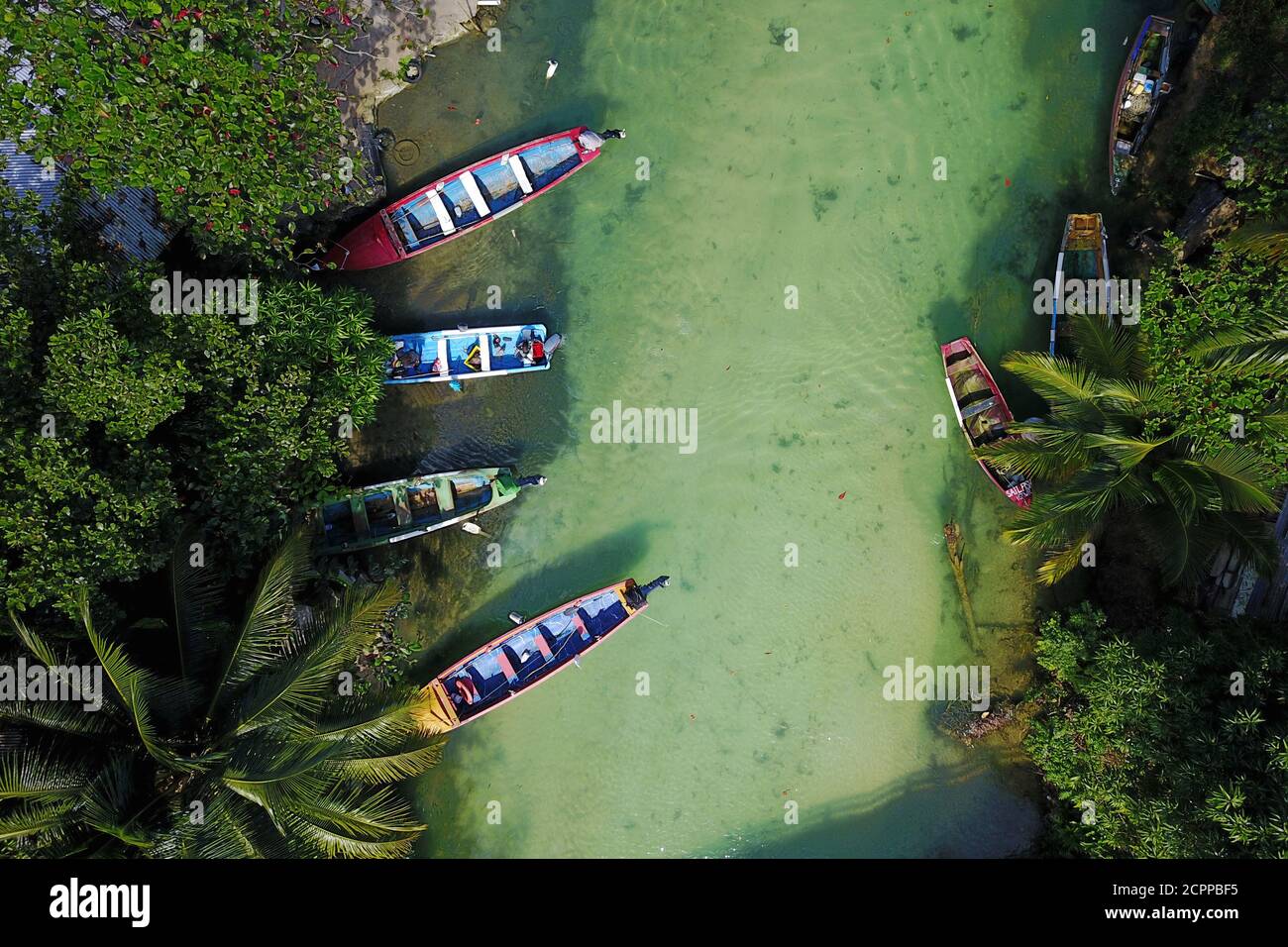 Aerial shot of White River, Ochos Rios, Jamaica with 4 colorful fishing boat moored in a small fishing settlement. Fishes are visible through the clea Stock Photo