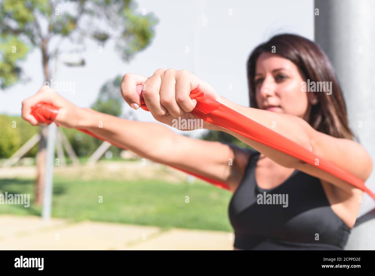 latin woman exercising using resistance bands with the help of light post on a green park. selective focus on right hand Stock Photo