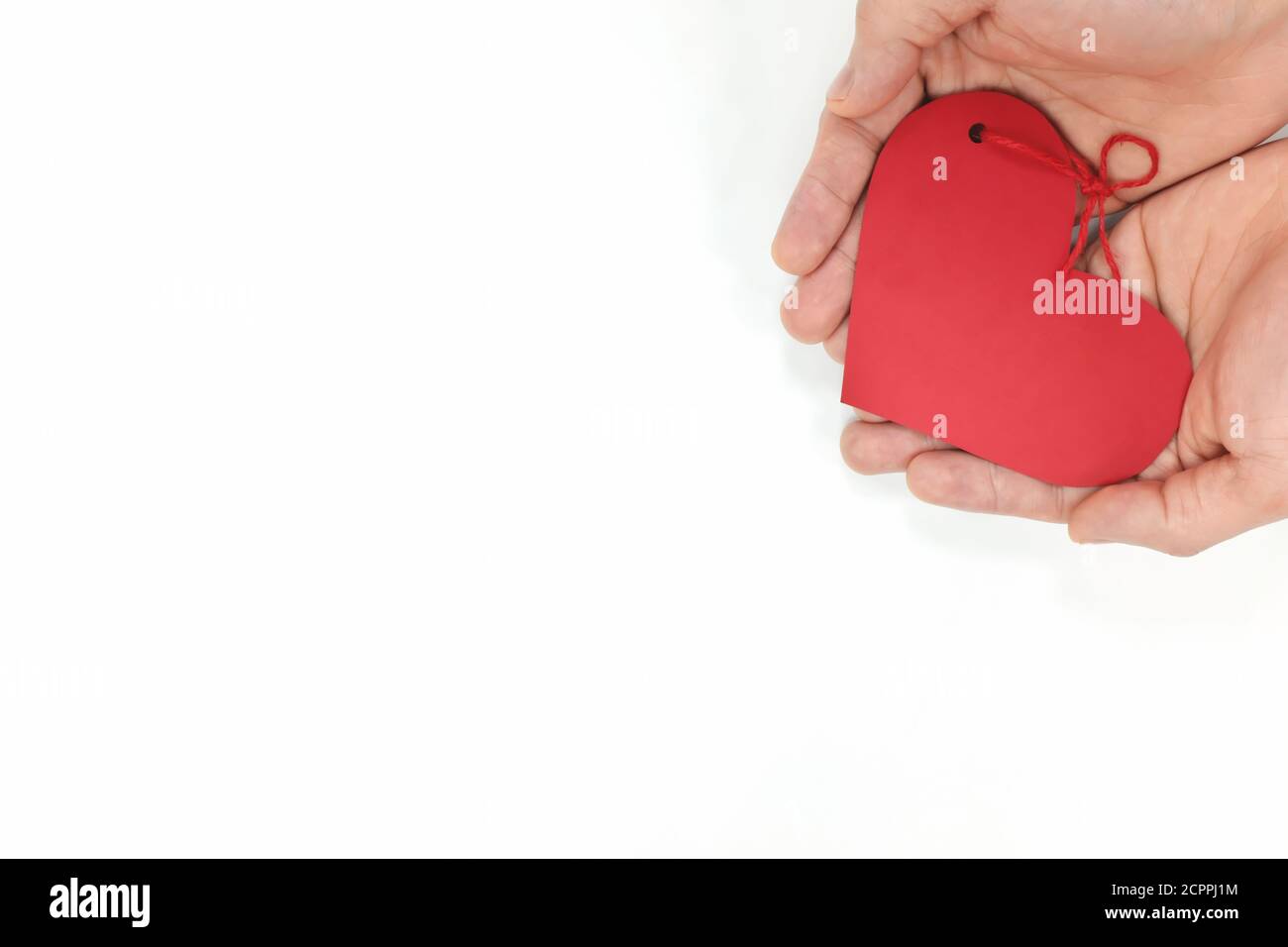 Top view of young male cupped hands holding a red heart shape tag in white background. Non-materialistic love is the best gift for birthday, christmas. Stock Photo