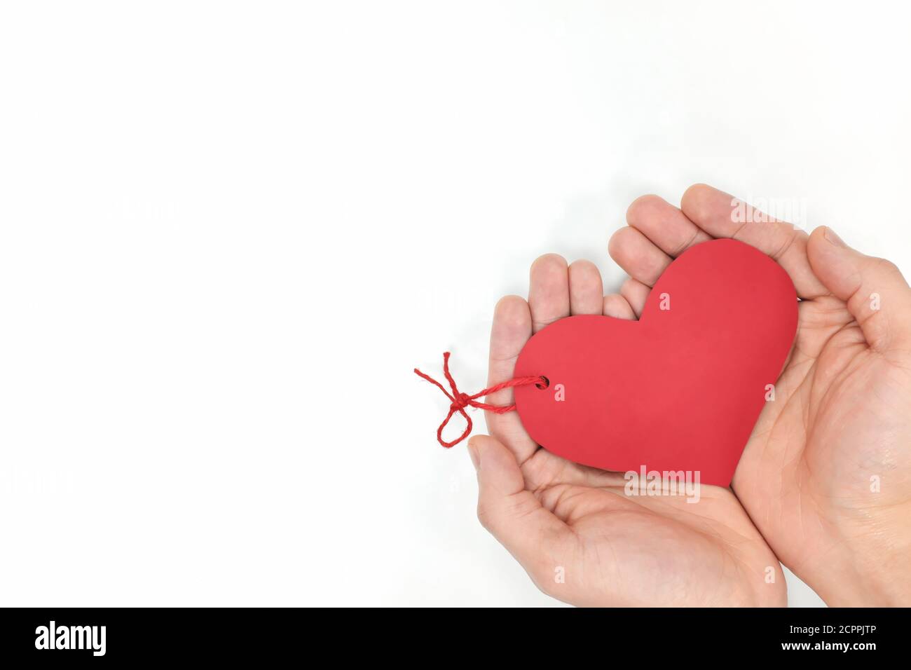 Top view of young male cupped hands holding a red heart shape tag in white background. Non-materialistic love is the best gift for birthday, christmas. Stock Photo