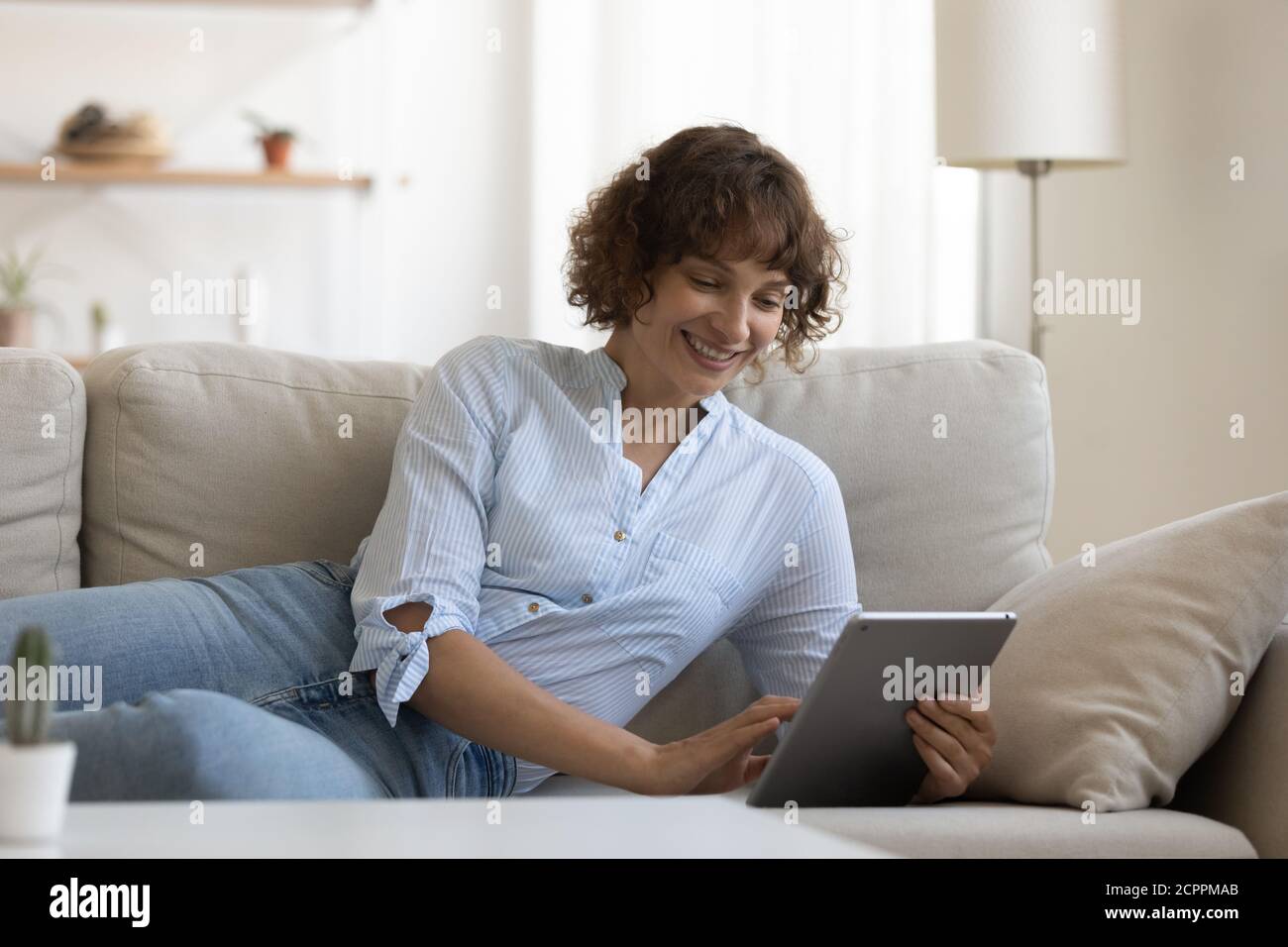 Smiling young woman relax on couch using tablet Stock Photo