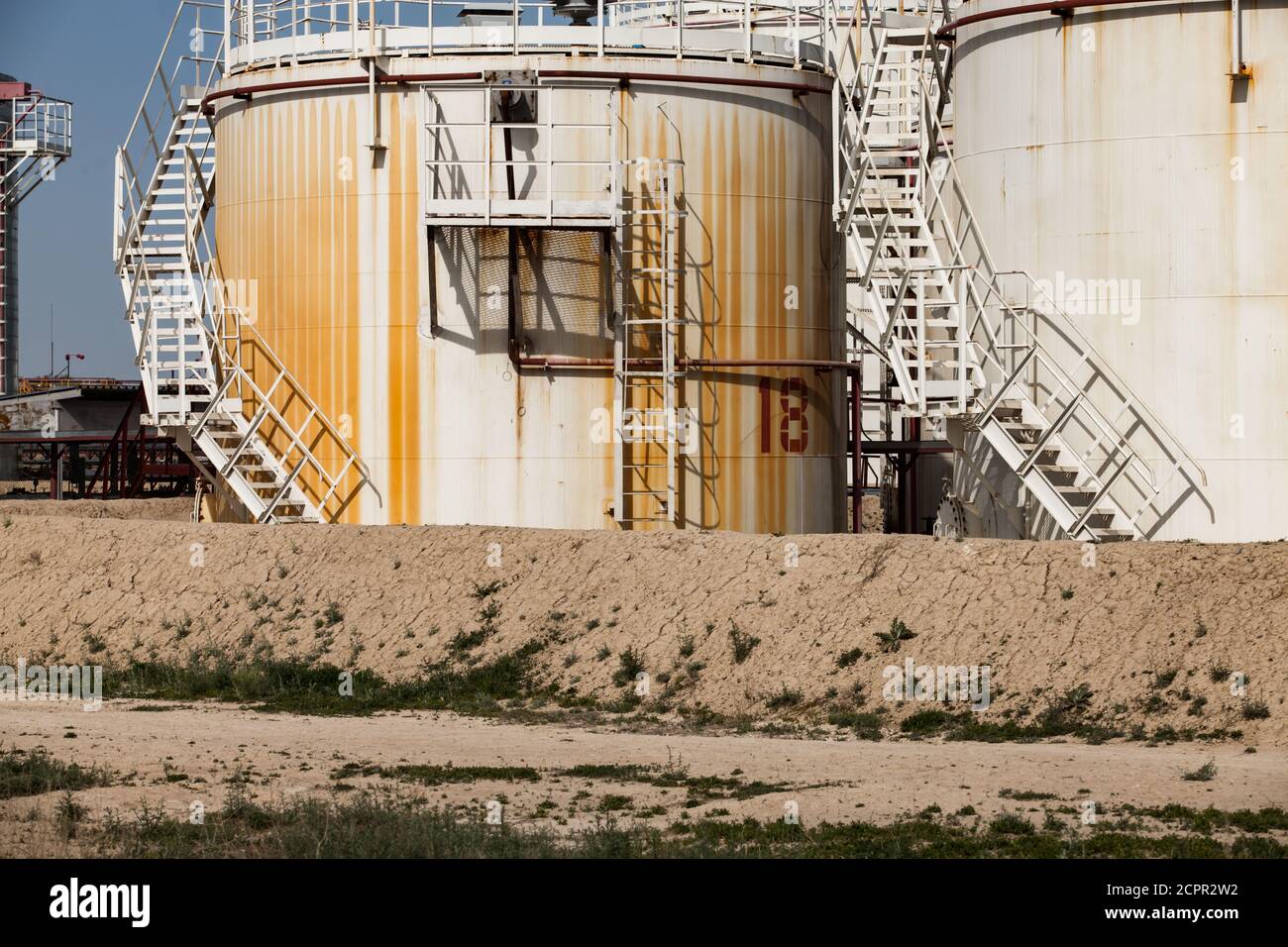 White and yellow oil storage tanks on bright sun on blue sky on oil refinery plant in desert. Close up. Stock Photo