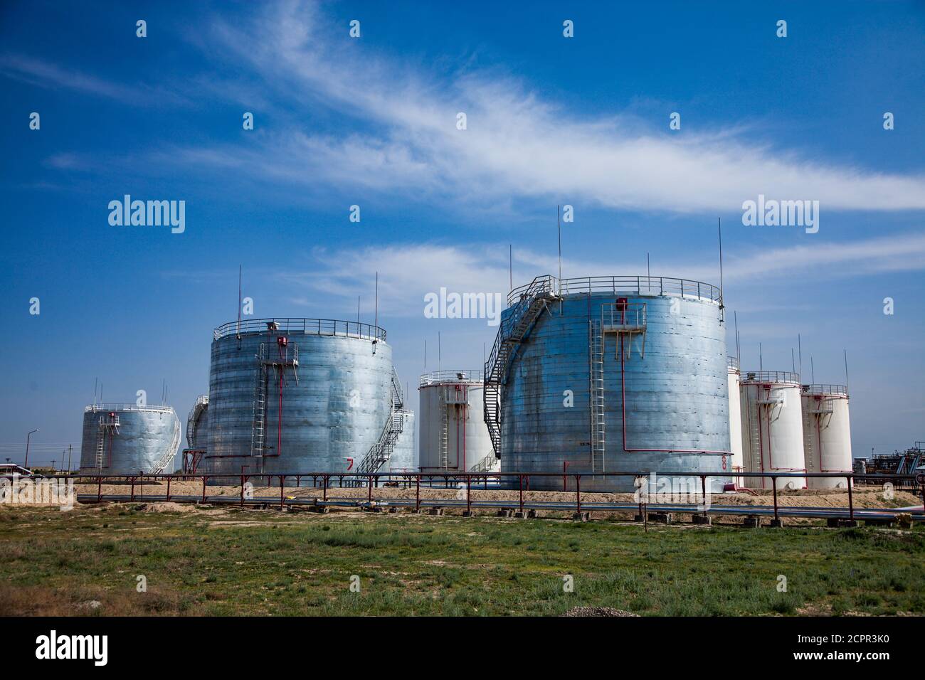 White and shiny metal oil storage tanks on bright sun. Oil refinery plant in desert. Near Taraz city. Against blue sky with light clouds. Panorama vie Stock Photo