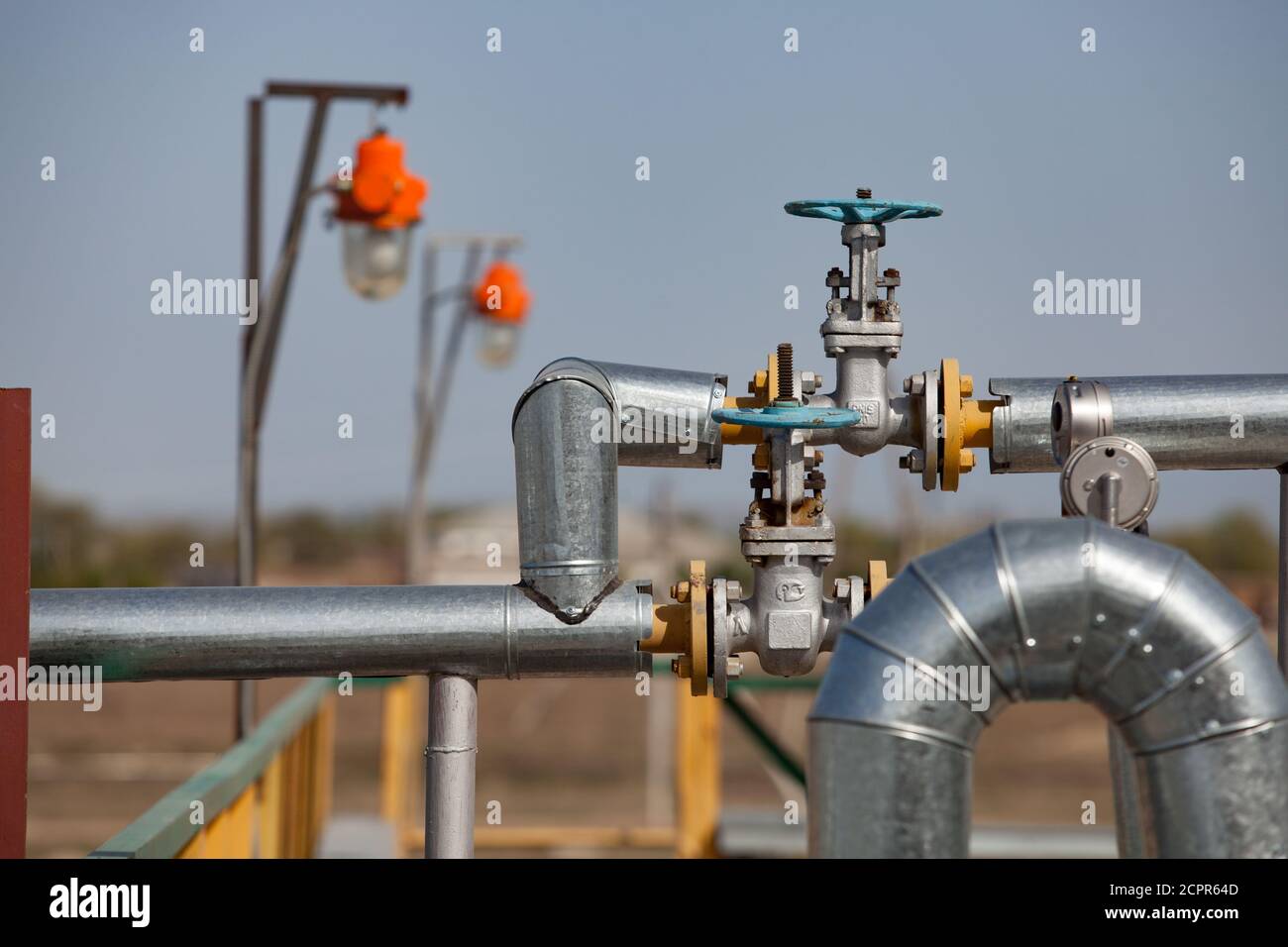 Oil refinery plant in desert. Valve armature and pipes on grey sky background. Focus on foreground. Stock Photo