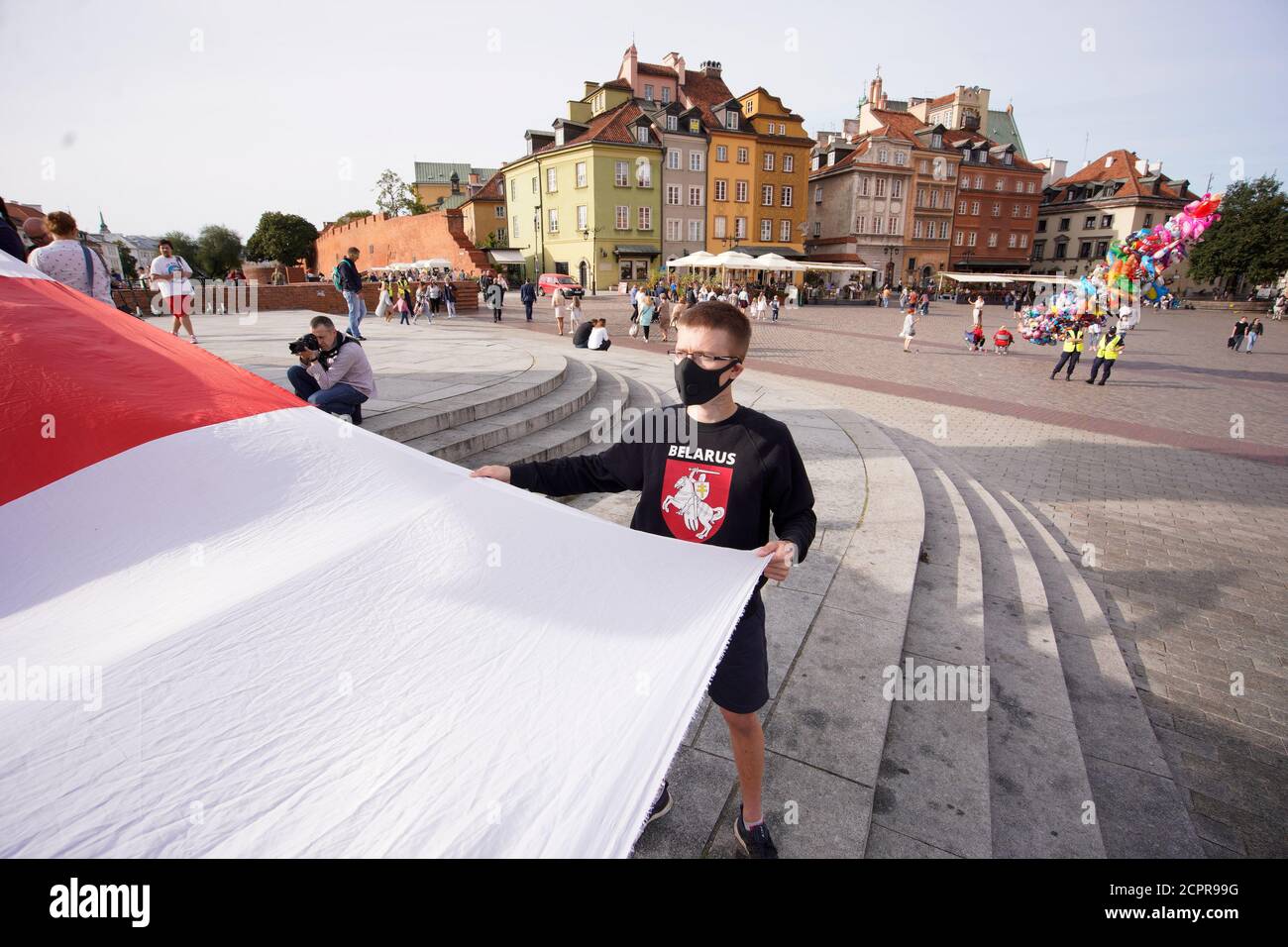 A man with a Pogon symbol on his sweater holds a large, Belarusian White-Red-White flag in Warsaw, Poland on September 19, 2020. Several dozen people, Stock Photo