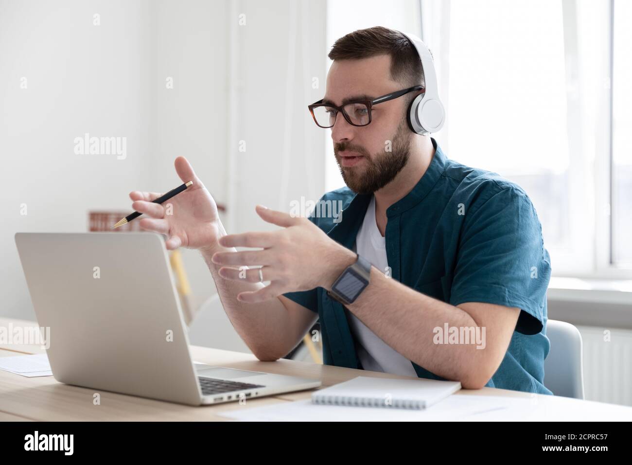 Serious businessman wearing headphones using laptop, speaking, making call Stock Photo