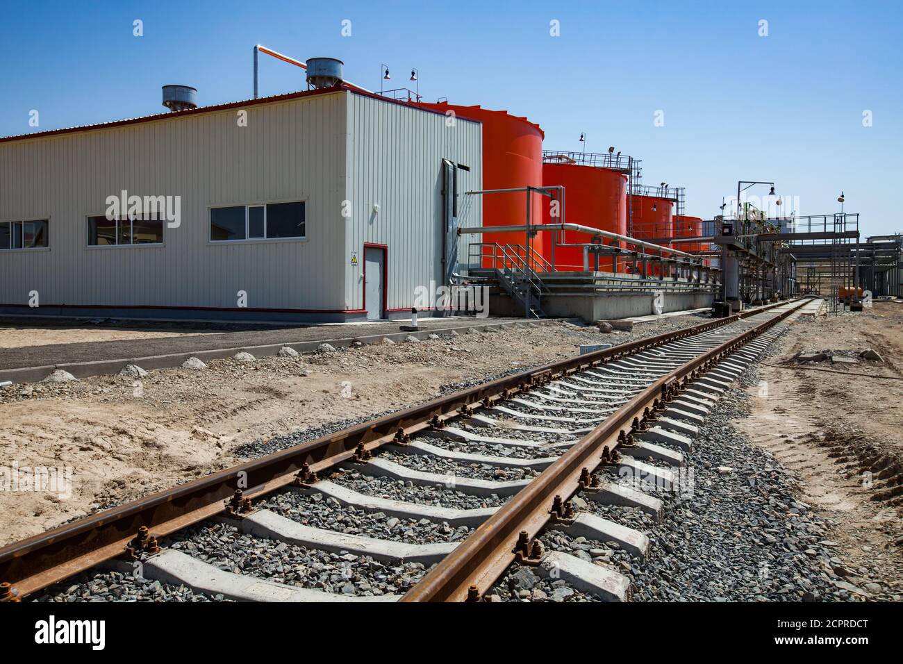Orange steel storage tanks with acid at (sulphuric) acid plant warehouse. Cargo train filling (loading) terminal. Stock Photo