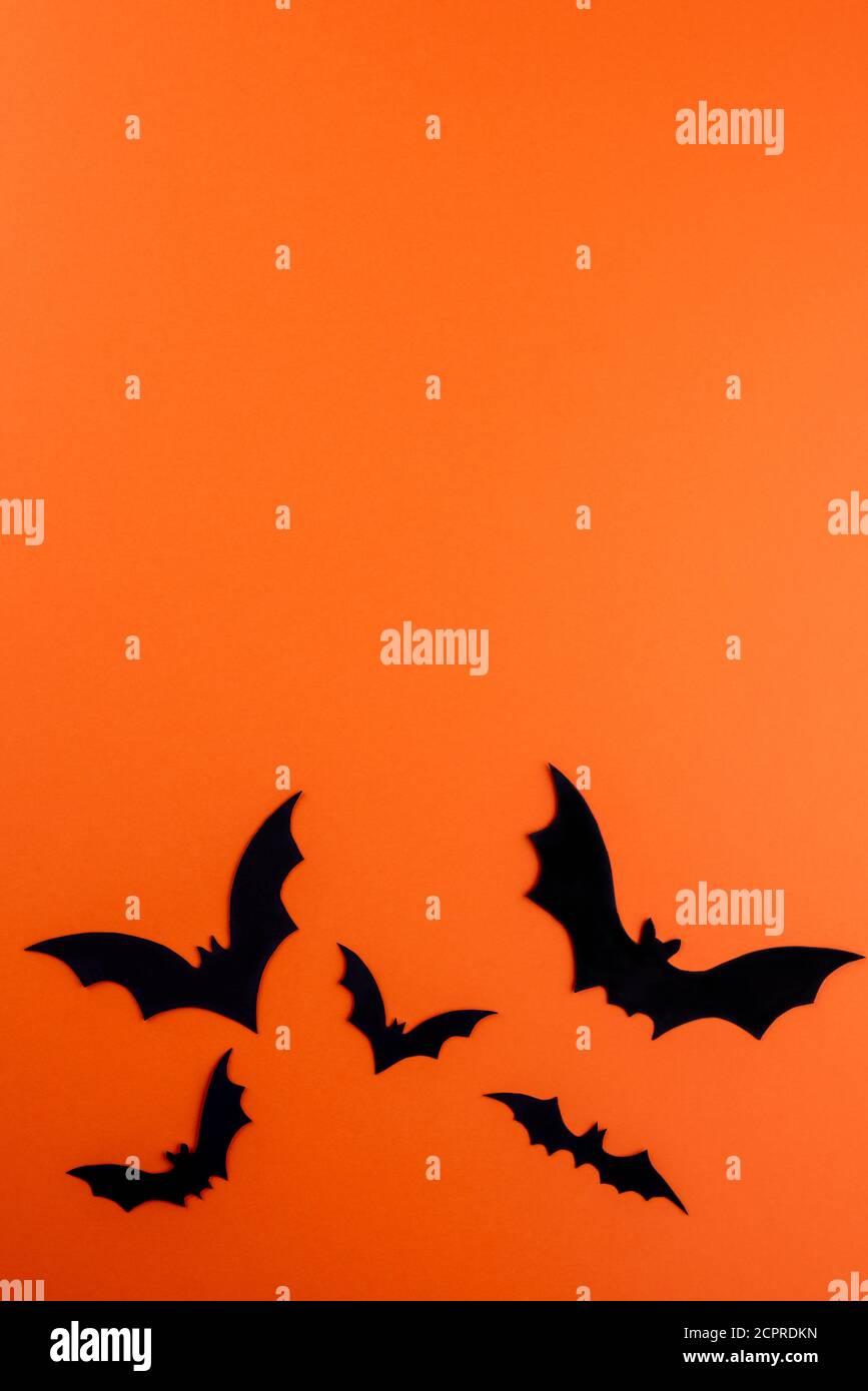 Few different large and small silhouettes of flying black bats on bright orange vertical paper background. Silhouettes are hand carved from cardboard. Stock Photo