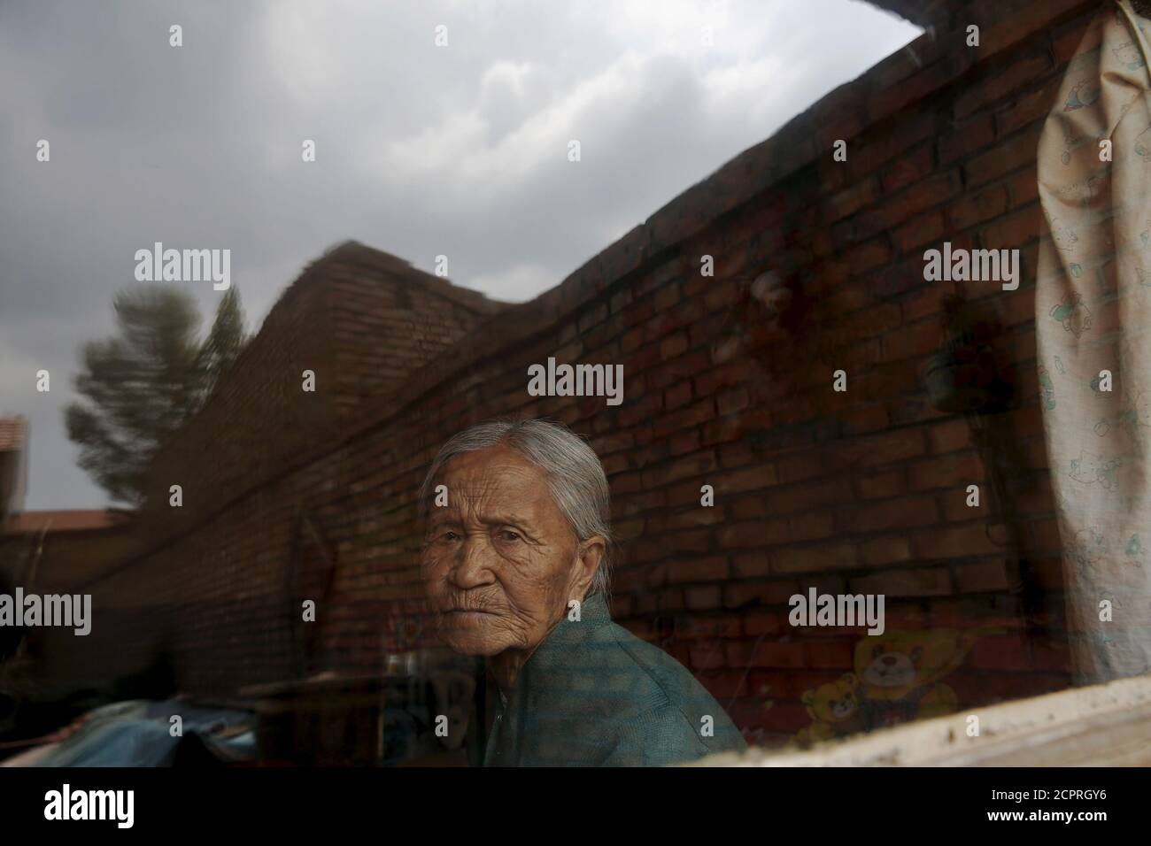 Former Chinese "comfort woman" Zhang Xiantu looks through the window of her house in Xiyan Town, Shanxi Province, China, July 18, 2015. “Comfort women� is the Japanese euphemism for women who were forced into prostitution and sexually abused at Japanese military brothels before and during World War Two. Zhang Xiantu is the only surviving "comfort woman" of the 16 plaintiffs in Shanxi who sued the Japanese government in 1995 for abducting girls and using them as "comfort women" during World War Two. According to information from China’s Commission of Inquiry into the Facts of Comfort Wome Stock Photo