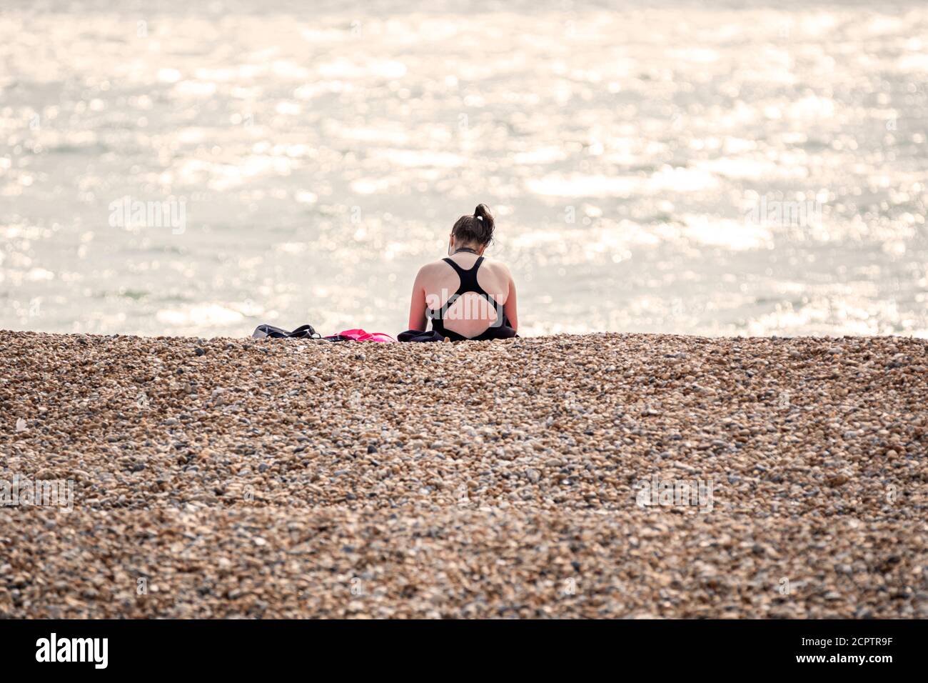 A woman sitting alone on a beach during covid-19 restrictions Stock Photo