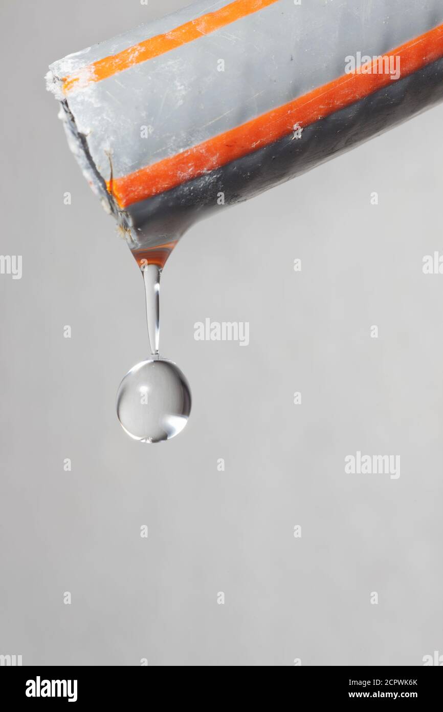 Extreme close-up of a water drop dripping out of a hose - grey background Stock Photo