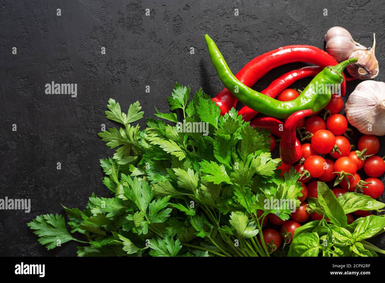 Fresh ingredients for cooking spicy sauce: cherry tomatoes, parsley, basil, garlic and chilli pepper on black background. Top view. Copy space Stock Photo