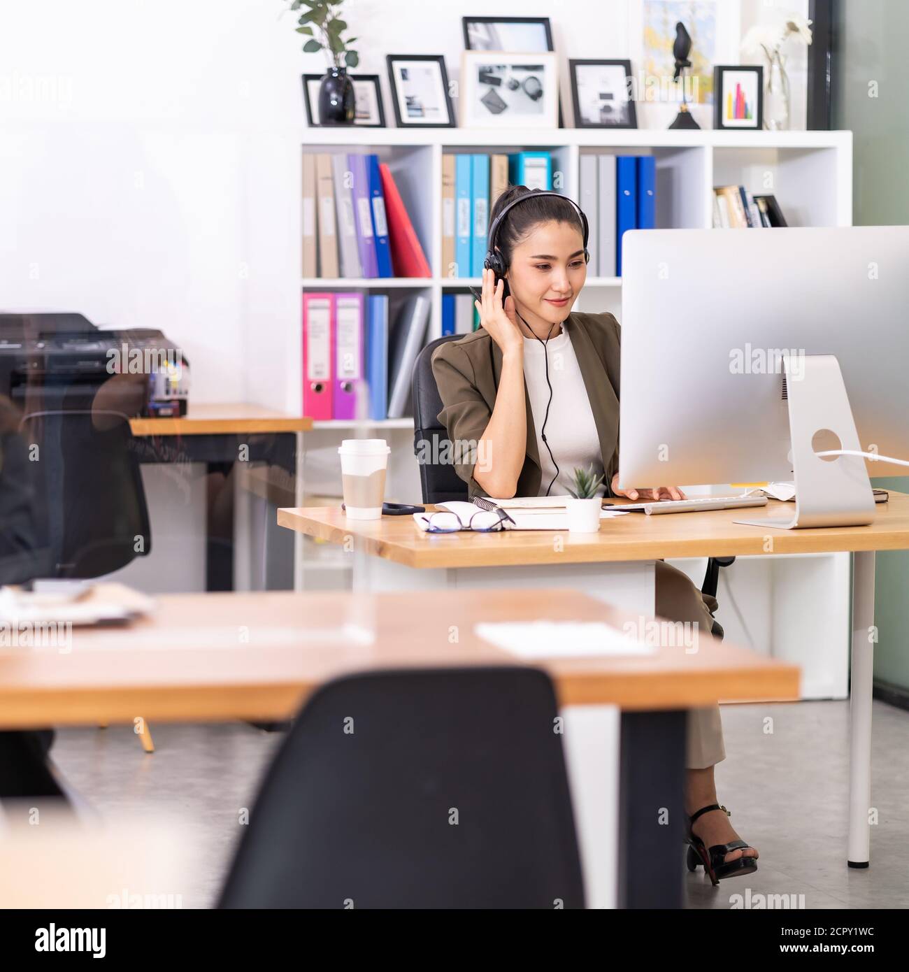 Young adult friendly confidence Asian woman with headsets working in a call center with social distance table as new normal practice. Call center and Stock Photo