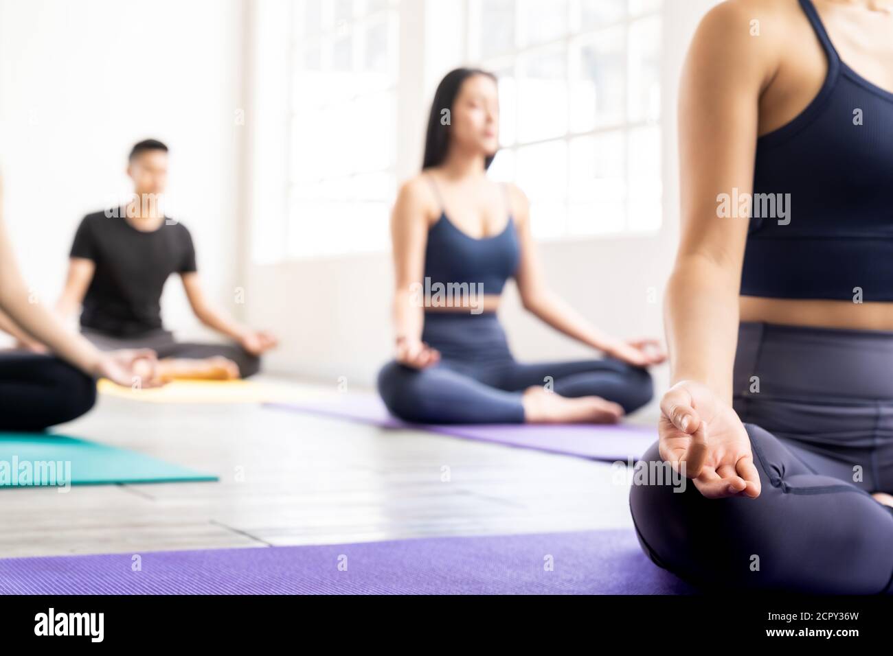 Close up of sporty attractive asian coach on Lotus pose position sitting Padmasana with background of student practicing yoga lesson. Work out fitness Stock Photo