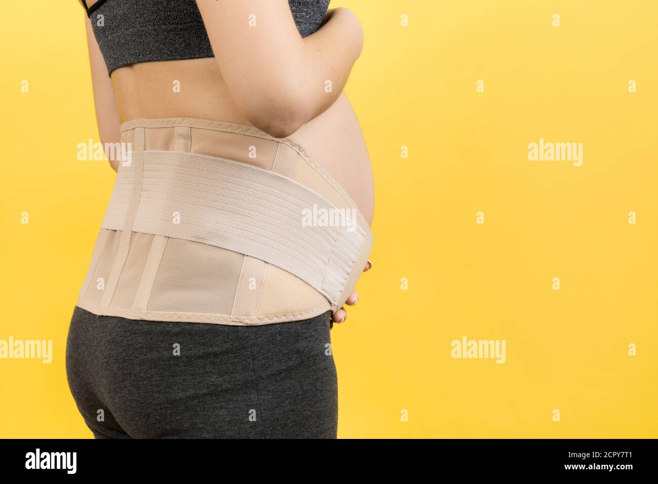Back view of pregnant woman wearing pregnancy belt at yellow background