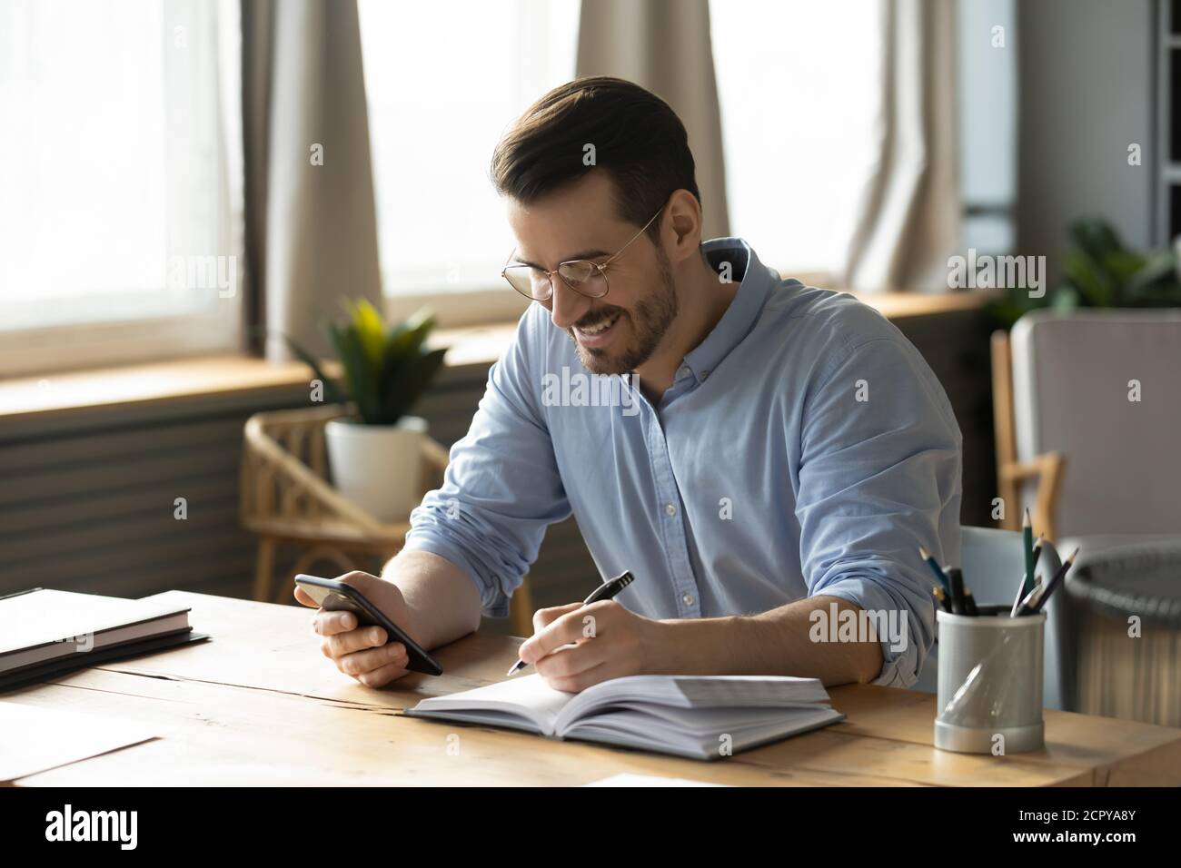 Smiling man use smartphone making notes planning Stock Photo