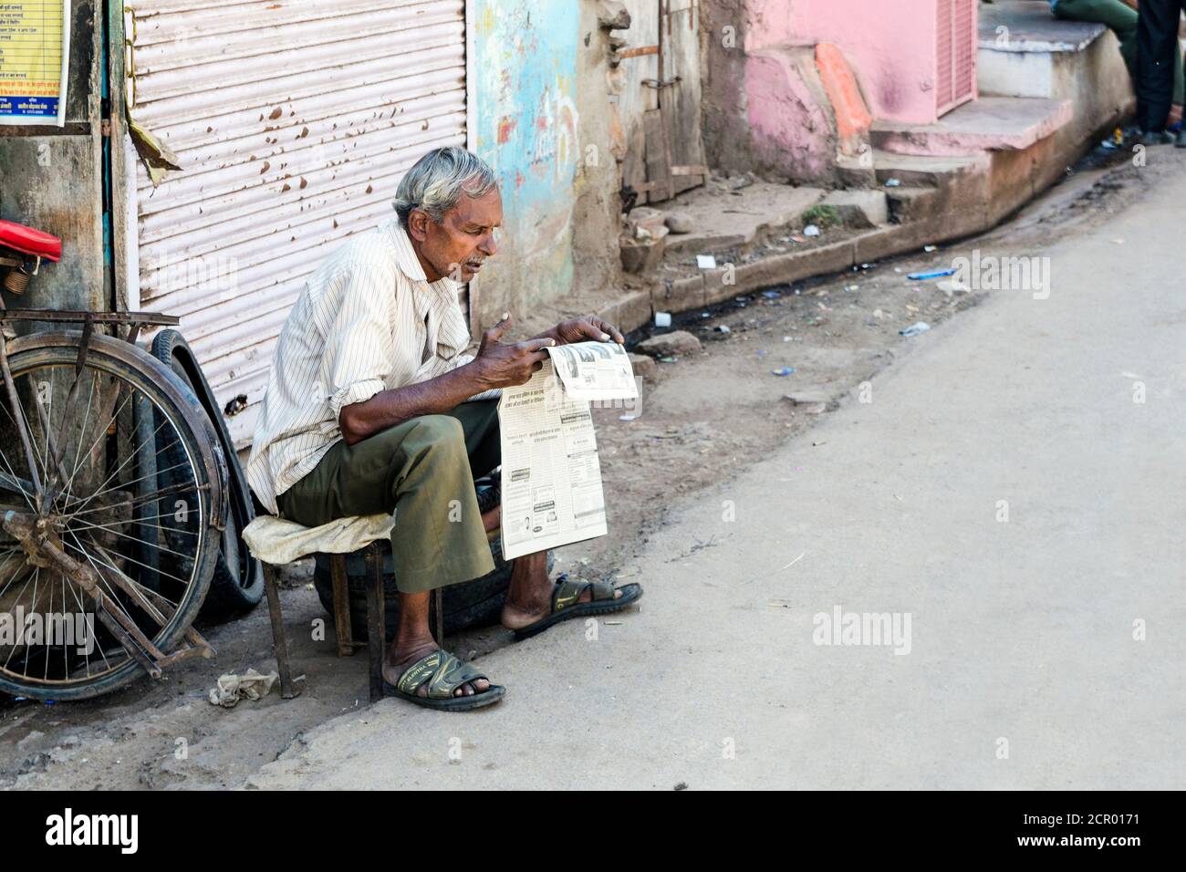 Old Indian man reading the newspaper at the side of the road, Bundi, India Stock Photo