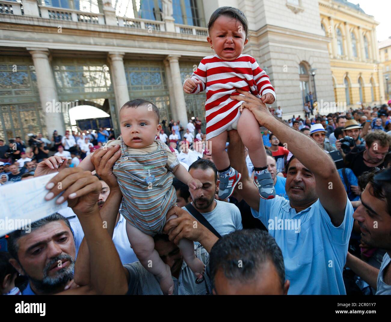 Migrants wave their train tickets and lift up children outside the main Eastern Railway station in Budapest, Hungary, September 1, 2015. Hungary closed Budapest's main Eastern Railway station on Tuesday morning with no trains departing or arriving until further notice, a spokesman for state railway company MAV said. There are hundreds of migrants waiting at the station. People have been told to leave the station and police have lined up at the main entrance, national news agency MTI reported.  REUTERS/Laszlo Balogh Stock Photo