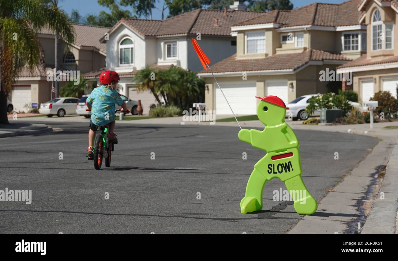 A sign urges drivers to go slow in a residential neighborhood, as a small child plays in the street. Stock Photo