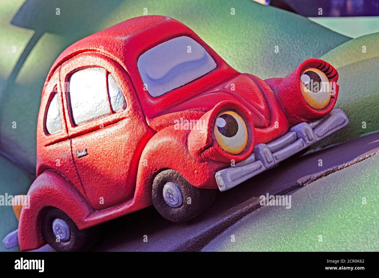 Anthropomorphic red toy car traveling on a green landscape Stock Photo
