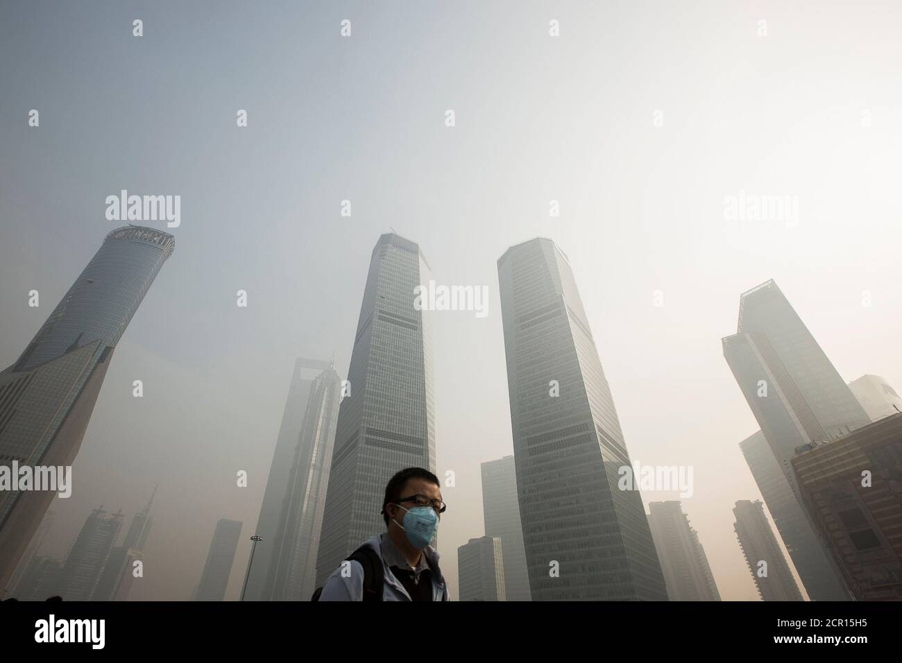 A man wears a mask while walking on a bridge during a hazy day in Shanghai's financial district of Pudong December 5, 2013. Hazardous air pollution forced schools to shut or suspend outdoor activities in at least two cities in eastern China, where residents complained of the yellow skies and foul smells that are symtomatic of the country's crippling smog crisis. Nanjing suspended classes in primary and secondary schools and Qingdao banned outdoor activities, said the official Xinhua news agency.   REUTERS/Aly Song  (CHINA - Tags: BUSINESS ENVIRONMENT) Stock Photo