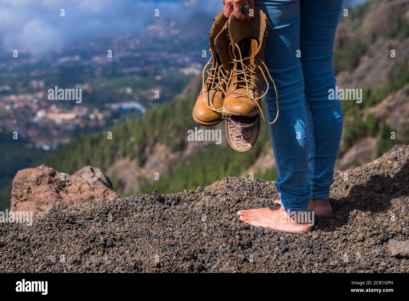 Travel and wanderlust lifestyle concept with barefoot woman stand up with broken shoes on hands looking at the view on the top of the mountain Stock Photo