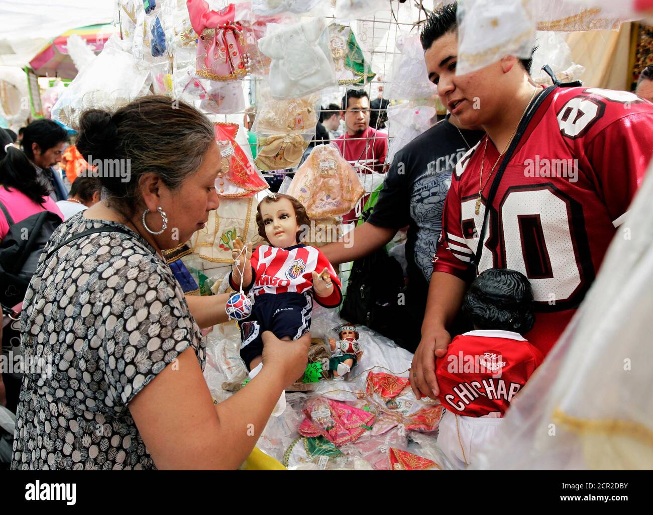 A customer (L) looks at a baby Jesus doll, dressed in a replica of club  Guadalajara Chivas' jersey, before "Candelaria Day" in Mexico City January  23, 2012. As part of tradition, February