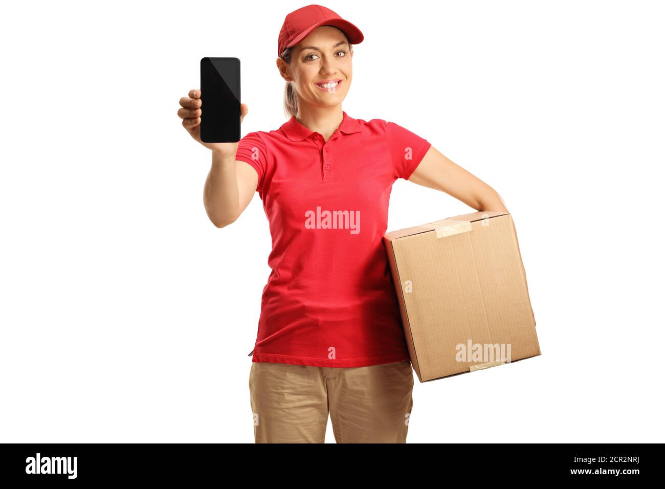 Female delivery worker in a red t-shirt holding a box and showing a mobile phone isolated on white background Stock Photo