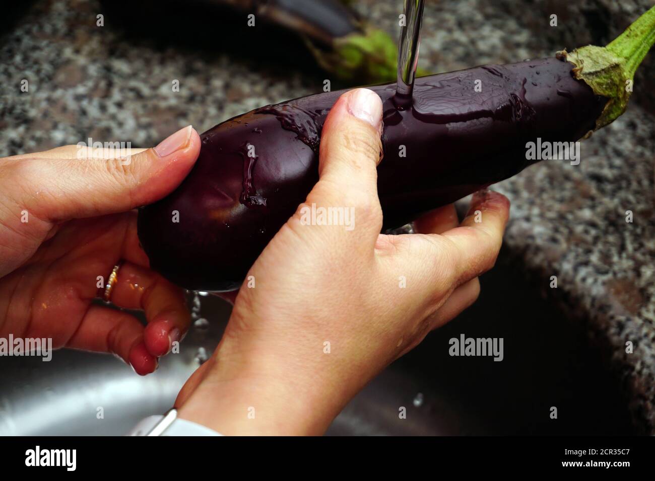 Woman washing eggplant under the faucet in the kitchen Stock Photo