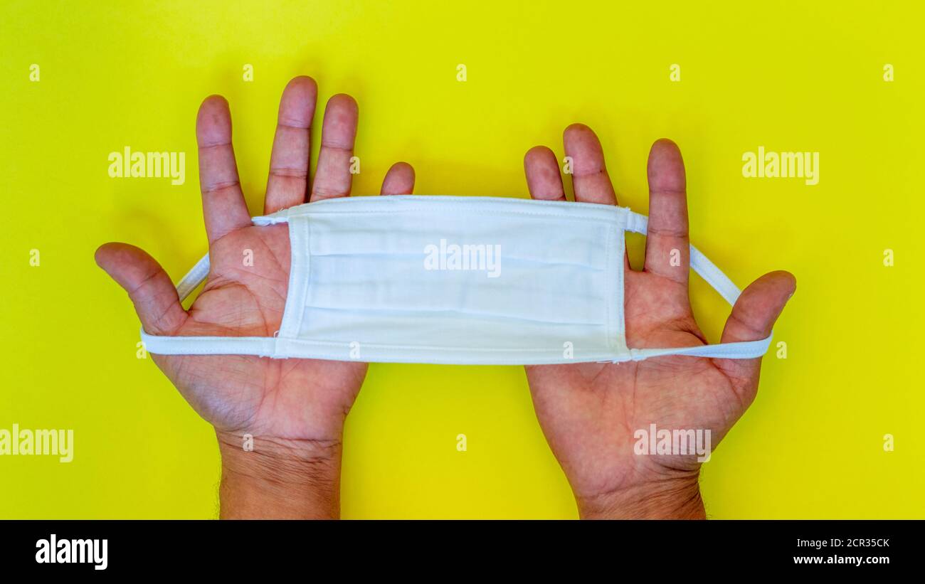Hands holding a white face mask on a yellow background. Public health Stock Photo