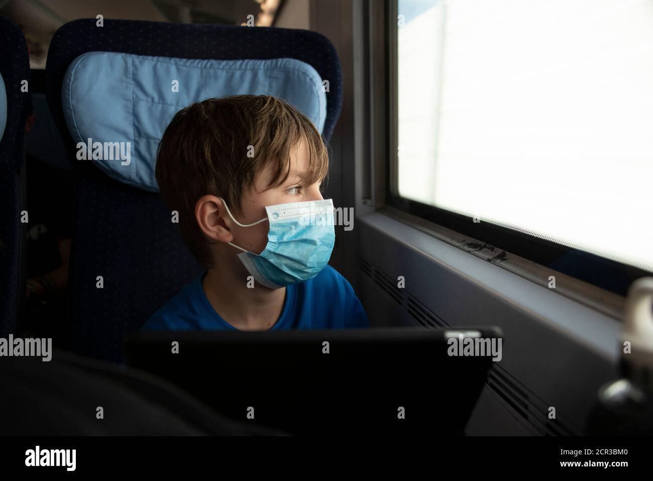 Boy sits in a train wearing a mask, respirator, medical mask, mouth and nose protection Stock Photo