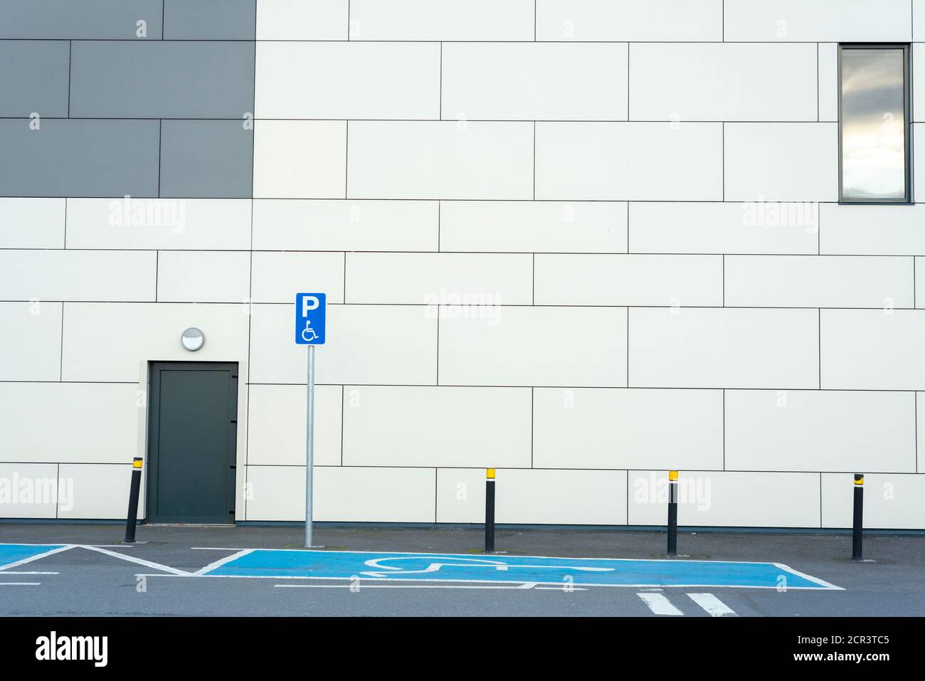 Empty disabled handicap parking space bay with blue marking and handicapped sign symbol by building wall. Stock Photo
