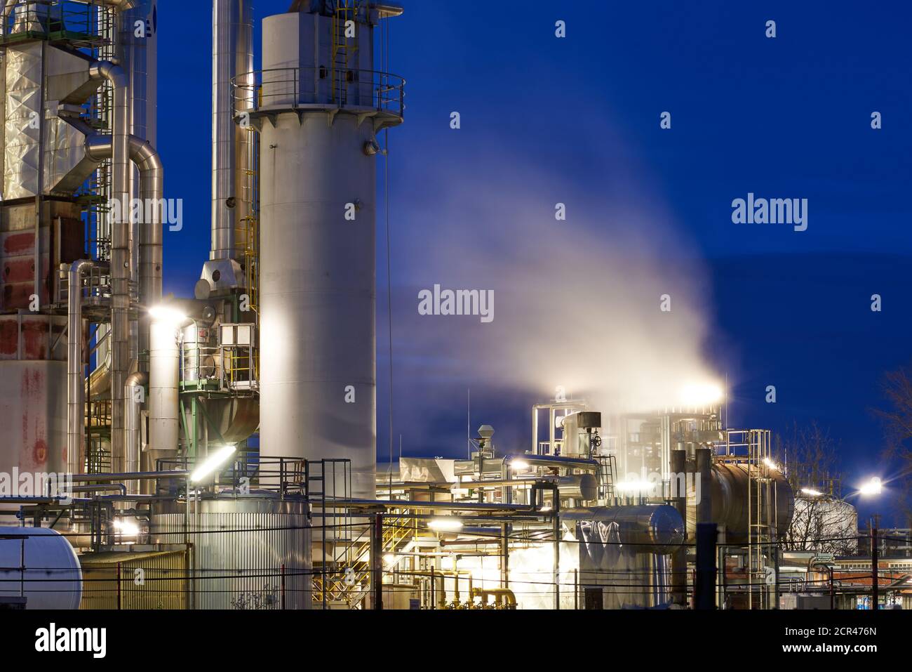 Petroleum refinery with a cooling tower and fog from free cooling after sunset with lights Stock Photo