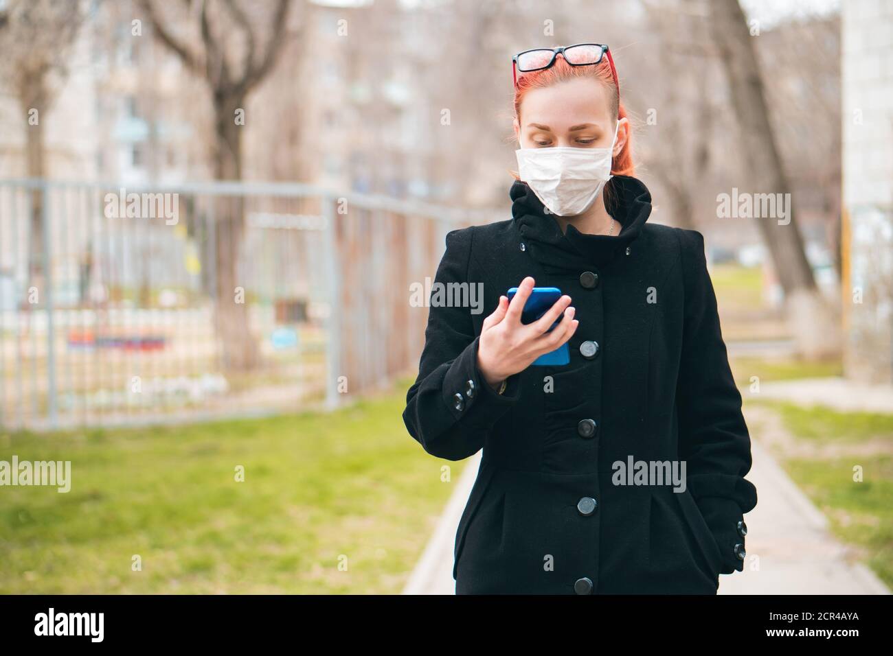 Young woman in medical mask looks at phone and reads news about virus. Epidemic protection concept with space for text. Stock Photo