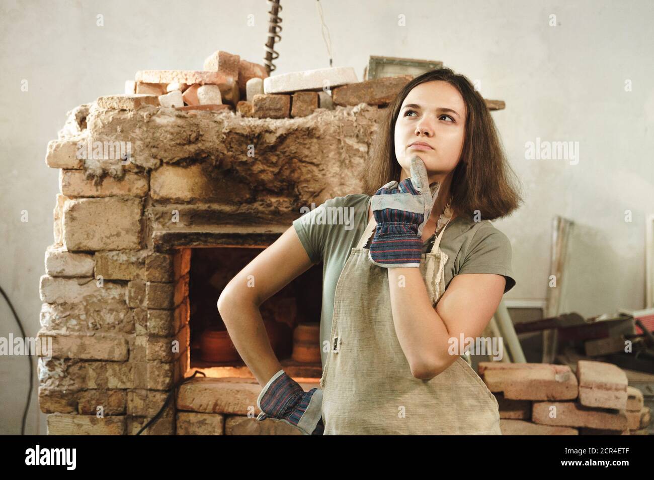 Potter girl with apron in workshop on background of pottery kiln ...