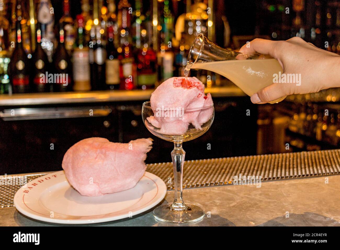 Demonstration of how to make a Pink Cashmere drink using a mix of juices and vodka poured over cotton candy. The liquids melt the cotton candy, creating a sweet after dinner drink. Stock Photo