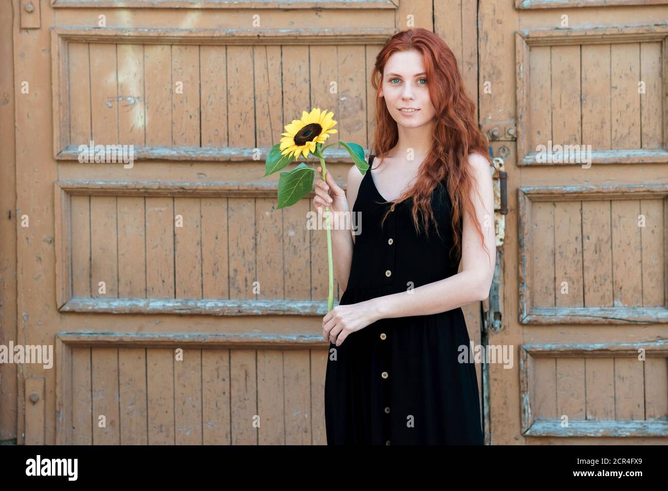 Girl with sunflower in hand on background of old wooden door. Simplicity and sincerity concept. Stock Photo