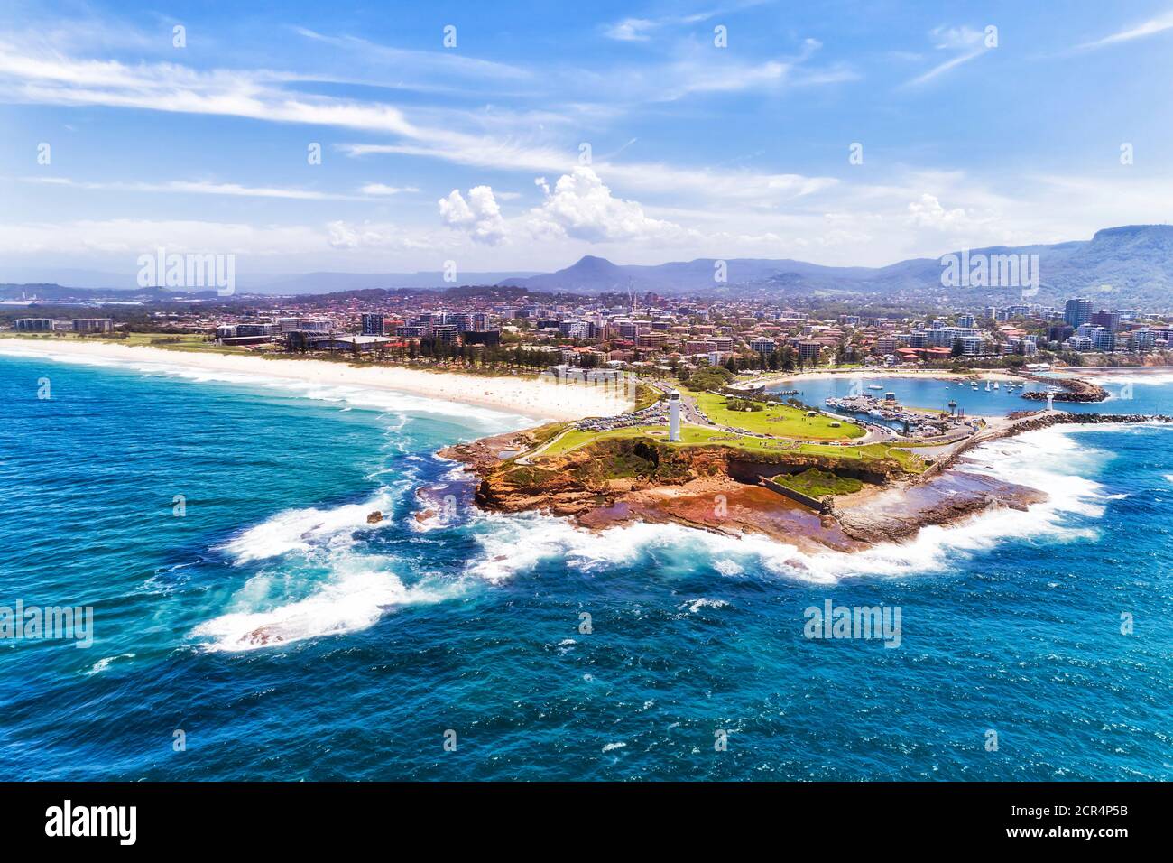 White lighthouse at the entrance to Wollongong harbour and marina port on coastal view from open sea - aerial. Stock Photo