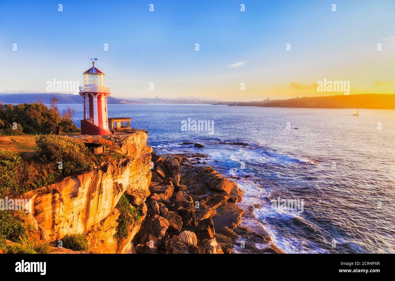 Warm rising sun light on HOrnby lighthouse and sandstone cliffs at entrance to Sydney harbour. Stock Photo