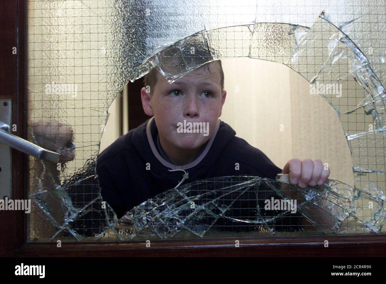 A young boy look outs though a smashed front door window following trouble with Loyalists attacking nationalists' homes in the Duncain Gardens area of north Belfast, Northern Ireland, June 21, 2002. Trouble flared at a sectarian interface during a controversial Orange Order parade in north Belfast where stones, bricks and other missiles were thrown over the peace line in Duncairn Gardens. Heavy rains put a damper on the first big march of the contentious Protestant marching season in Belfast on Friday, with just half the expected marchers showing up. REUTERS/Paul McErlane  PM/CRB Stock Photo