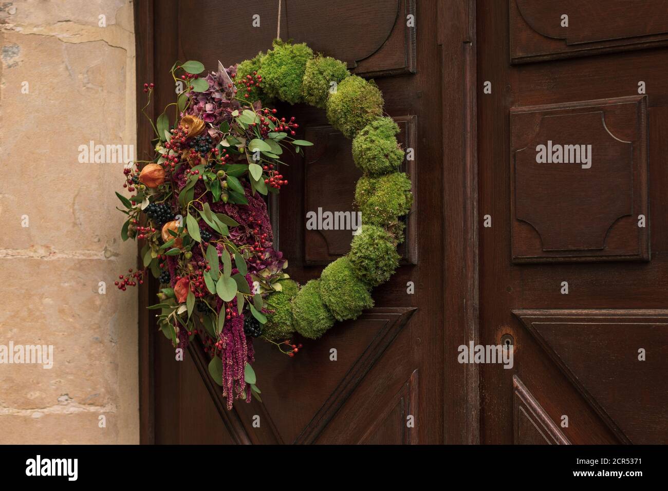 Wreath with the red berries and dry leaves hanging on a door. Stock Photo