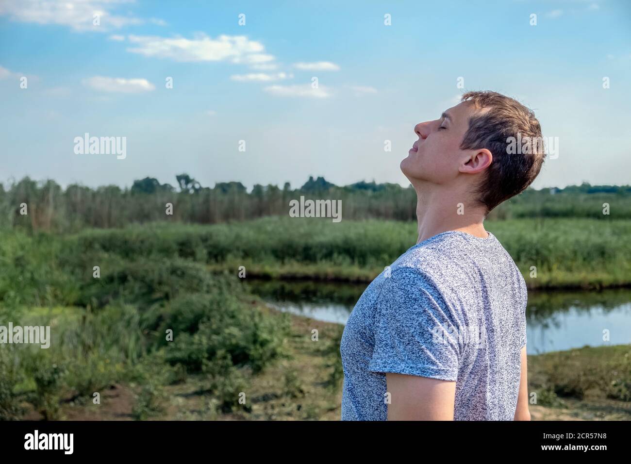 Happy casual man breathing fresh air in a field with lake in the background Stock Photo