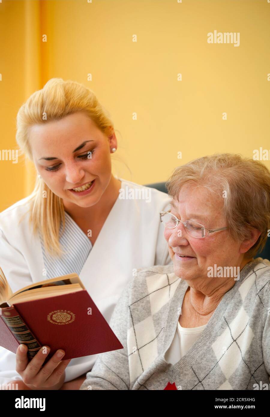 Generations in dialogue. In the day clinic of a geriatric unit, a patient is cared for during everyday exercises by a young woman doing voluntary Stock Photo