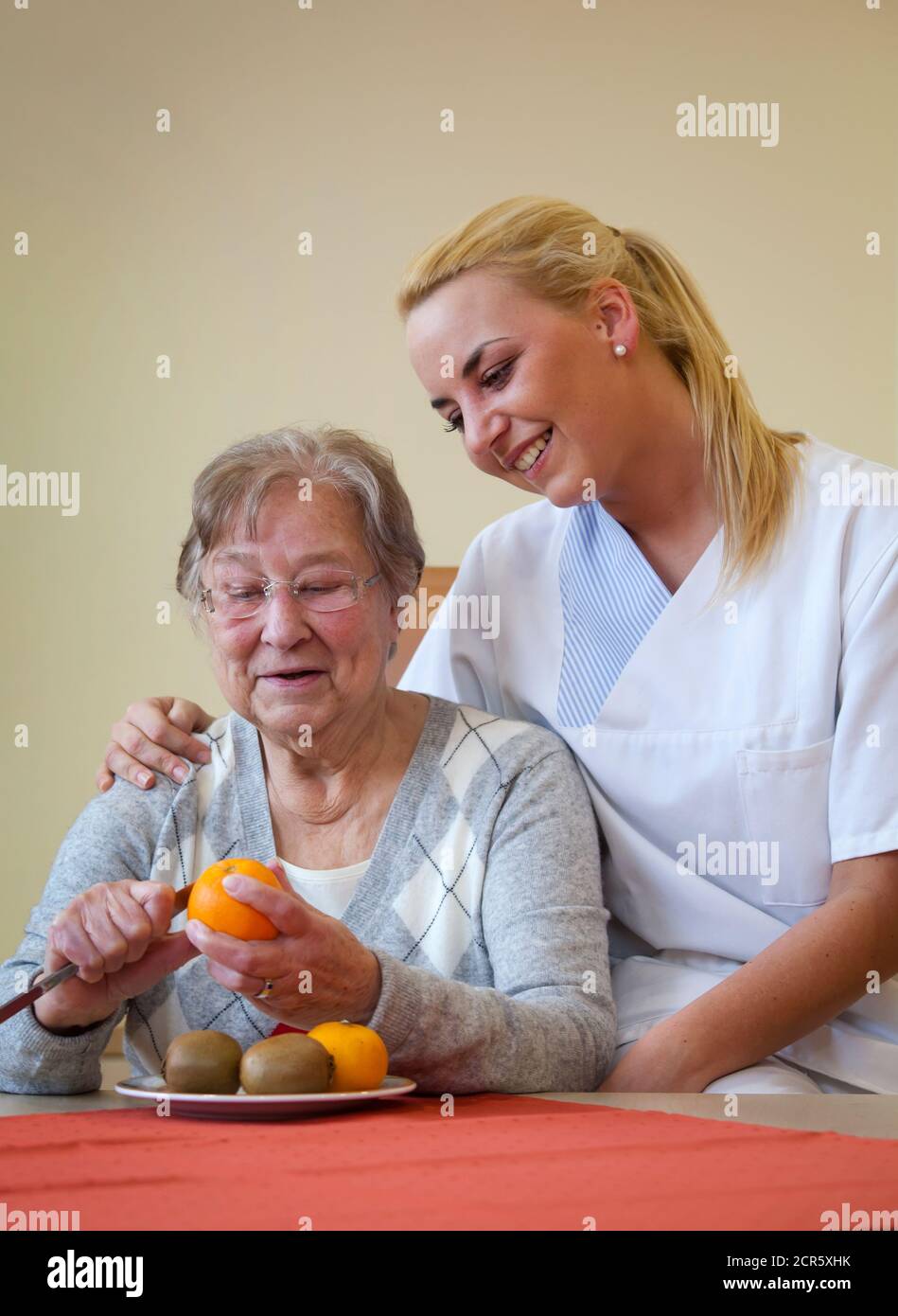 Generations in dialogue. In the day clinic of a geriatric unit, a patient is cared for during everyday exercises by a young woman doing voluntary Stock Photo