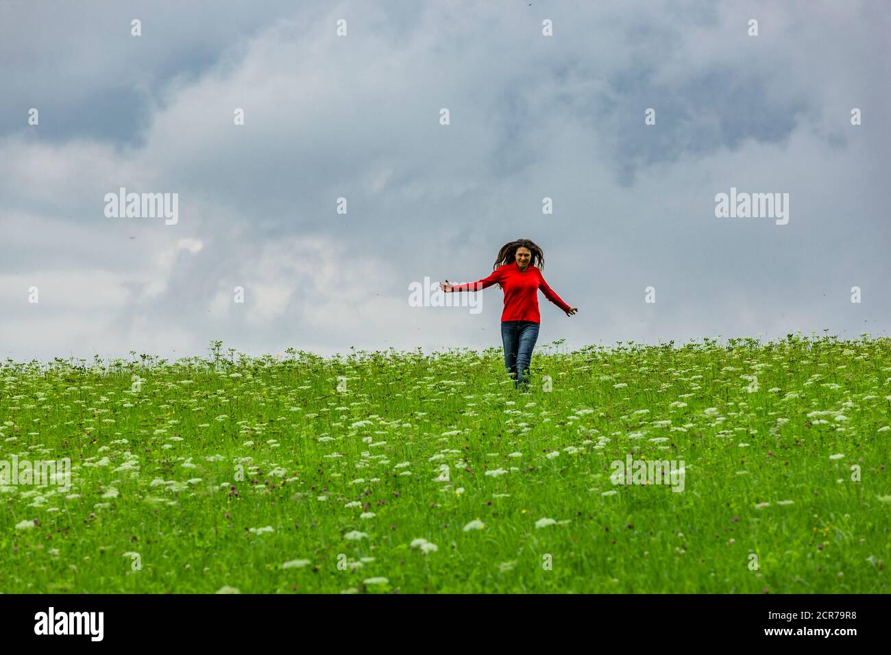Woman with red sweatshirt jumps in green meadow Stock Photo