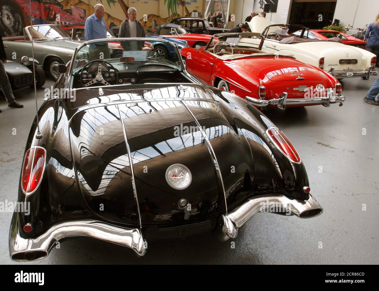 People stand behind a 1958 Chevrolet Corvette convertible (front LtoR), a  1962 Mercedes 190 SL roadster car and a 1960 Mercedes 220 SE cabriolet car  during an auction at the Oldtimer Galerie