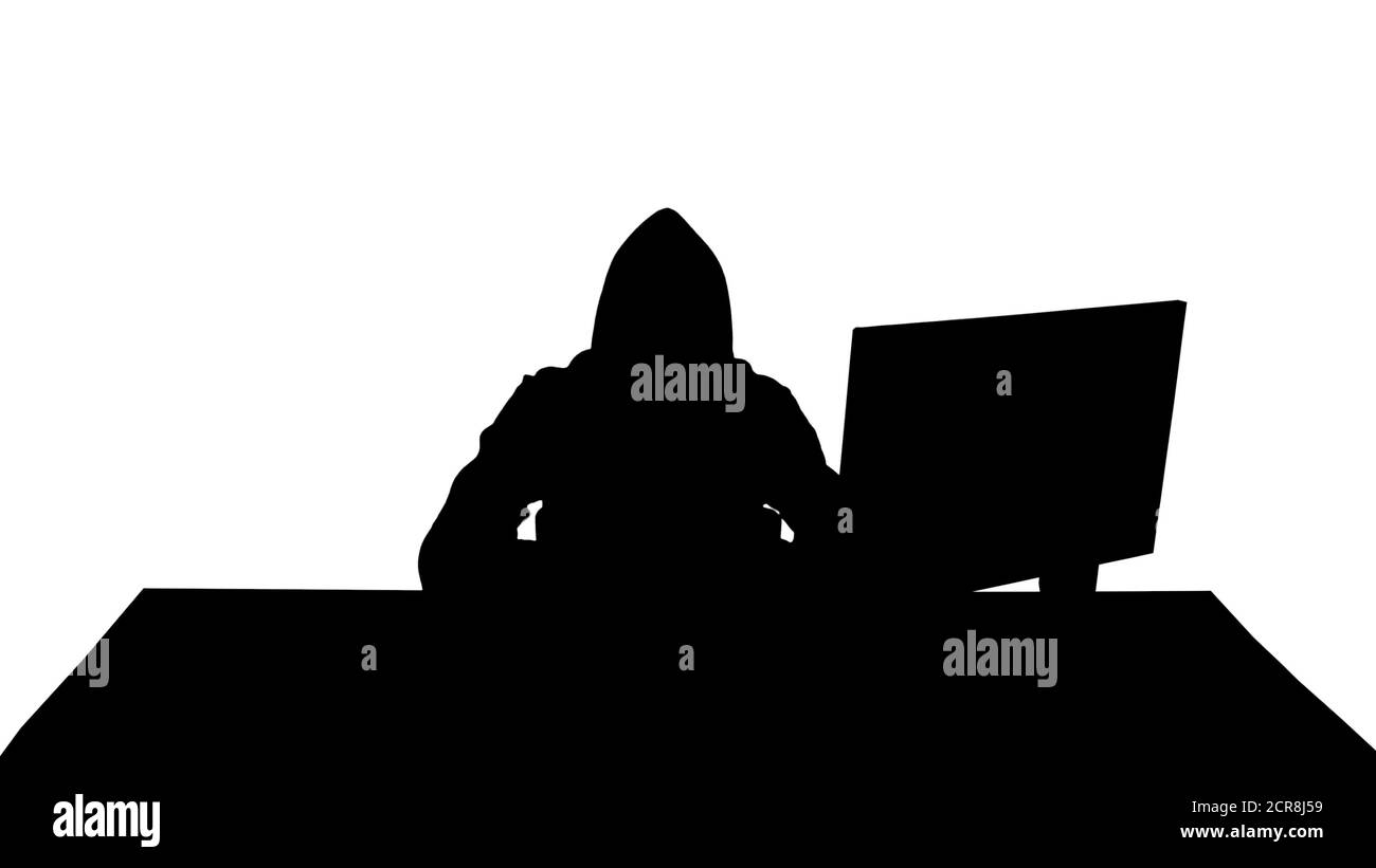 Silhouette Hooded hacker using laptop and smartphone. Stock Photo