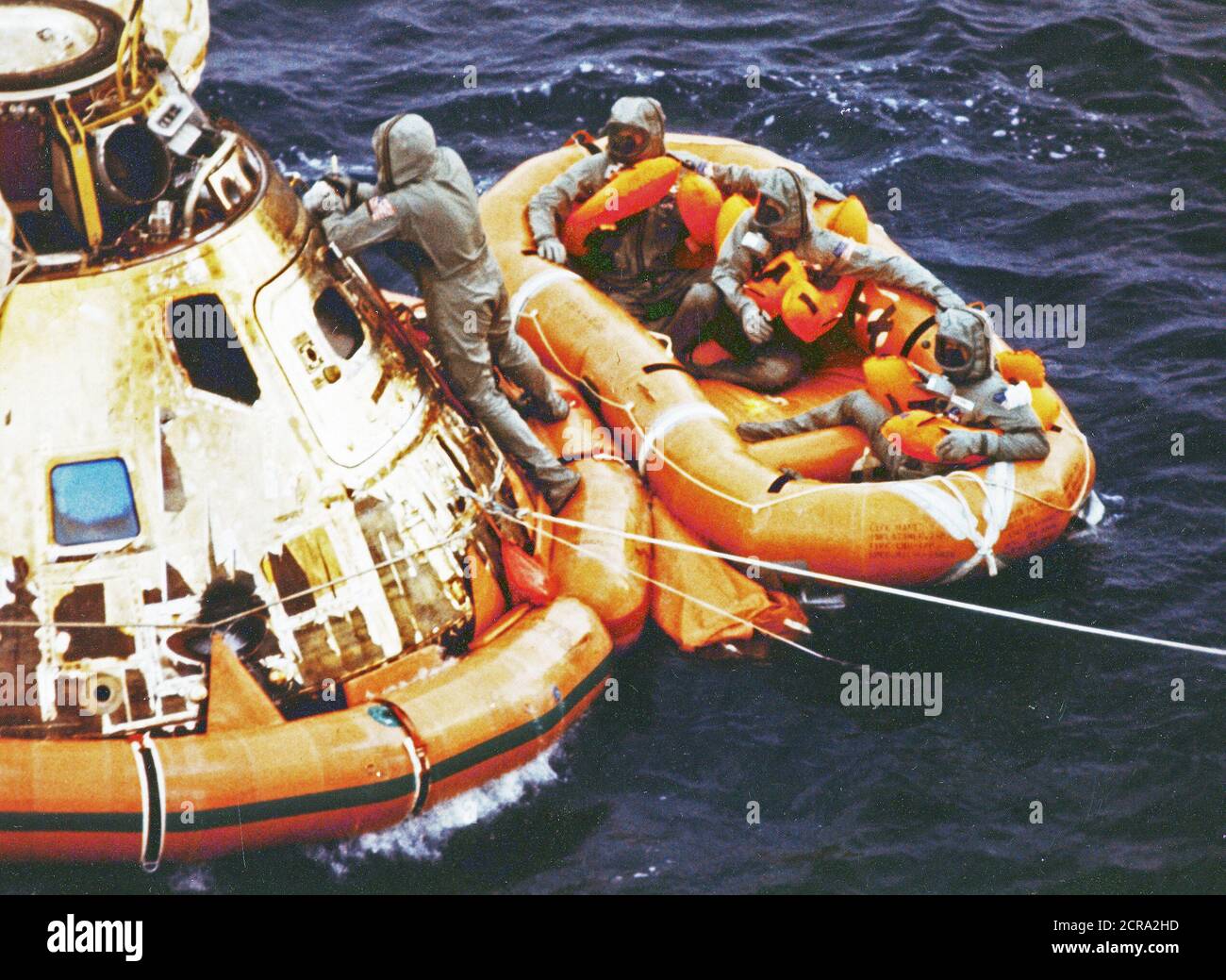 Pararescueman Lt. Clancy Hatleberg closes the Apollo 11 spacecraft hatch as astronauts Neil Armstrong, Michael Collins, and Buzz Aldrin, Jr., await helicopter pickup from their life raft. They splashed down at 12:50 pm EDT July 24, 1969, 900 miles southwest of Hawaii after a successful lunar landing mission. Stock Photo
