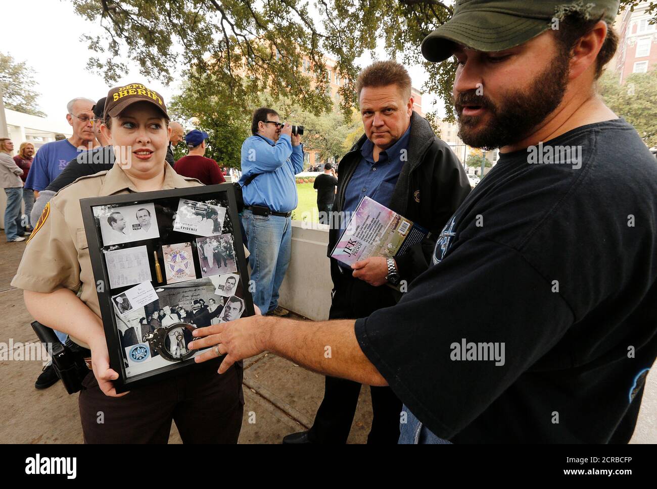 Jim Driscoll (R) talks about artefacts from the killing of Kennedy assassination suspect Lee Harvey Oswald held in a 'historical shadow box' being held by his wife, Armstrong County Sherriff's Deputy Carrie-Anne Driscoll (L) as they stand at the top of the infamous 'Grassy Knoll', near the spot of the 1963 assassination of U.S. President John F. Kennedy, in Dallas November 21, 2013. The shadow box, which concentrates on the role of Dallas Police homicide Detective Jim Leavelle, who was handcuffed to Oswald when Oswald was shot, is being raffled off to benefit a '100 Club' charity that looks af Stock Photo