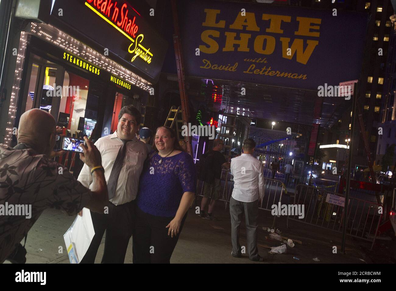 People pose for a photo as workers remove the marquee from the Ed Sullivan Theater where "The Late Show" with David Letterman used to tape in the Manhattan borough New York May 27, 2015. The taping and broadcast of the final edition of "The Late Show" was May 20, and workers are now slowly transforming the theater for the show's new host Stephen Colbert which will premiere on September 8, 2015. REUTERS/Carlo Allegri Stock Photo